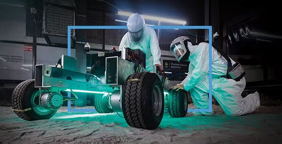 Two people in protective suits work on a rover in the Exolith Lab